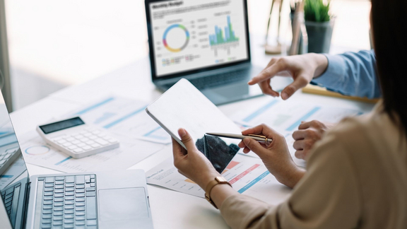 Schreibtisch mit PC, Taschenrechnung und Händen die über statistischen Auswertungen sind